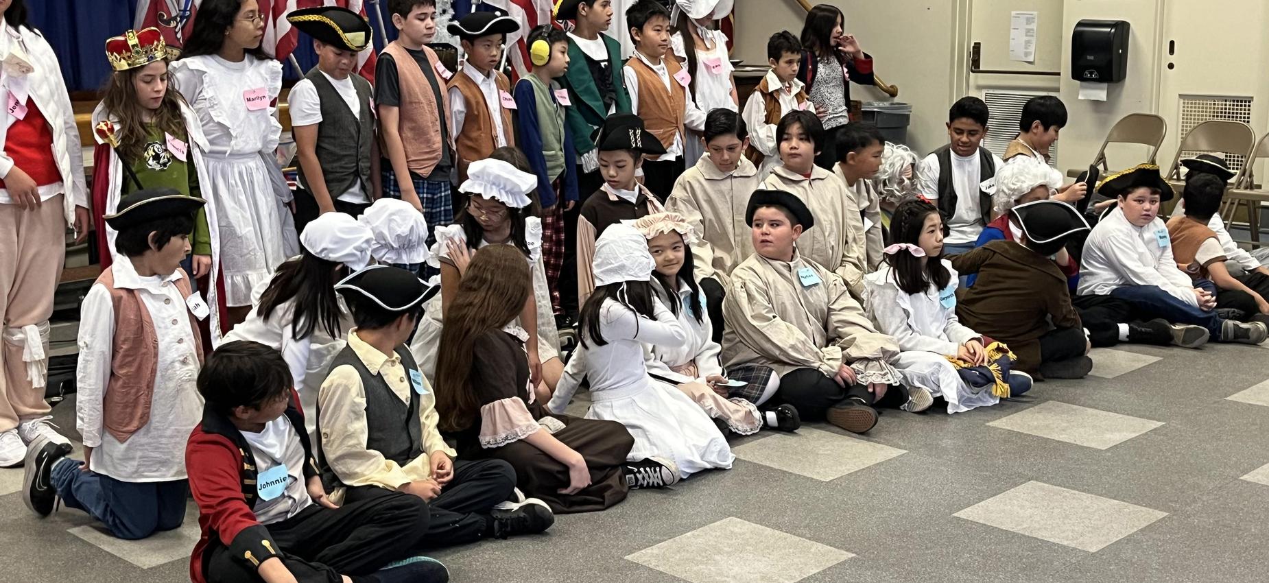 A group of children dressed in various historical costumes sitting together on the floor.