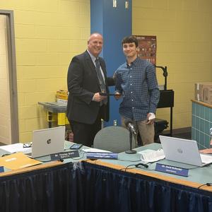 superintendent in suit shakes hand of senior in button up shirt and khakis