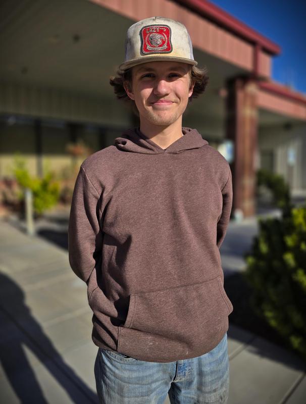 Young man in a ball cap and hoodie standing and smiling with his hands behind his back