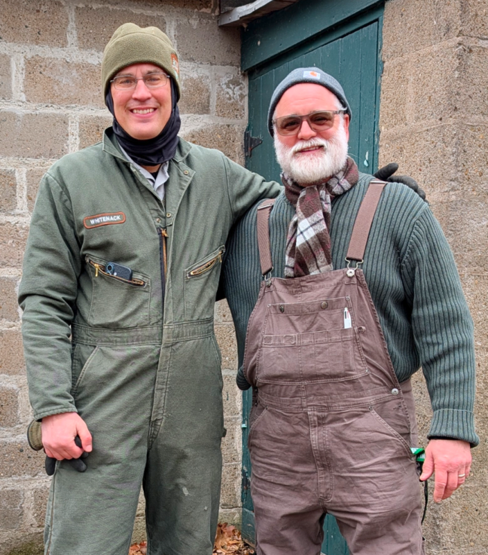 two men stand next to each other against a brick wall backdrop
