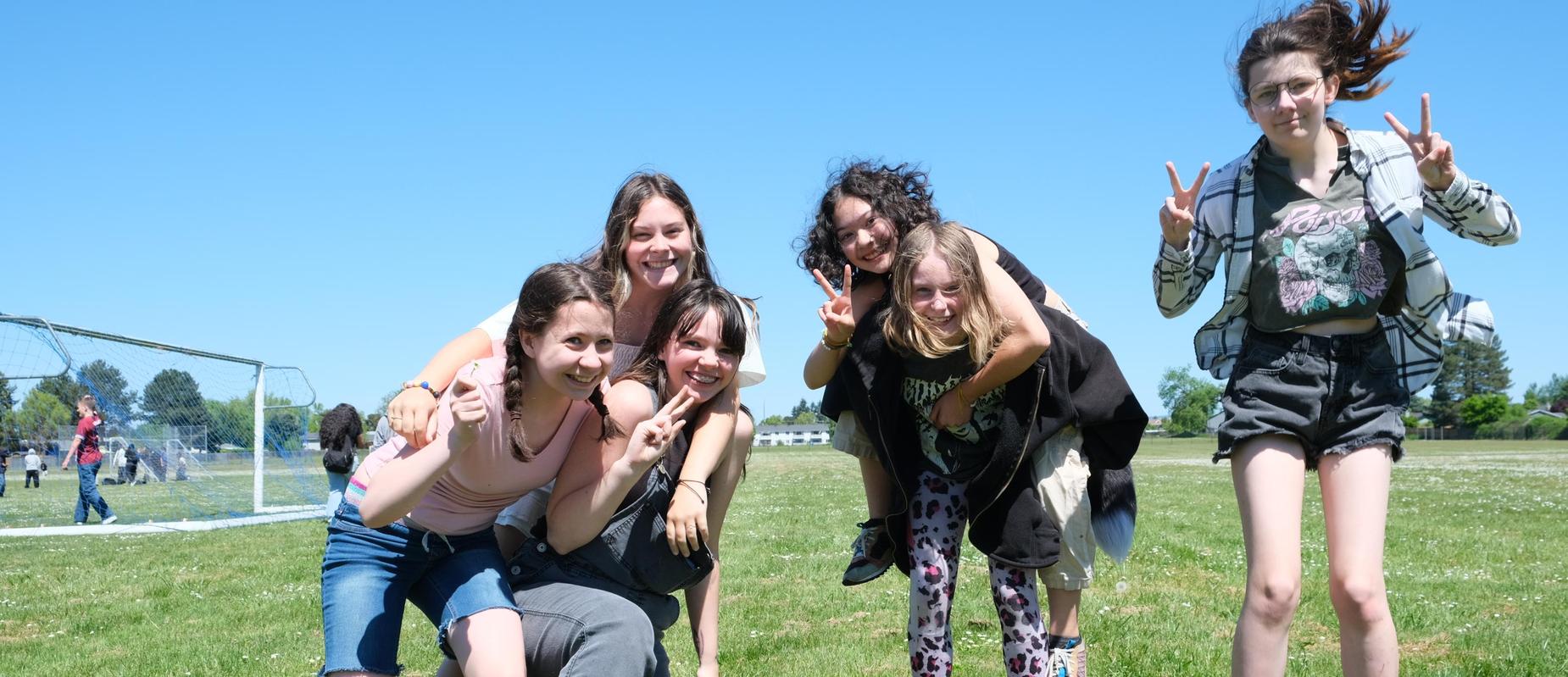 A group of six smiling friends posing together outdoors on a sunny day.