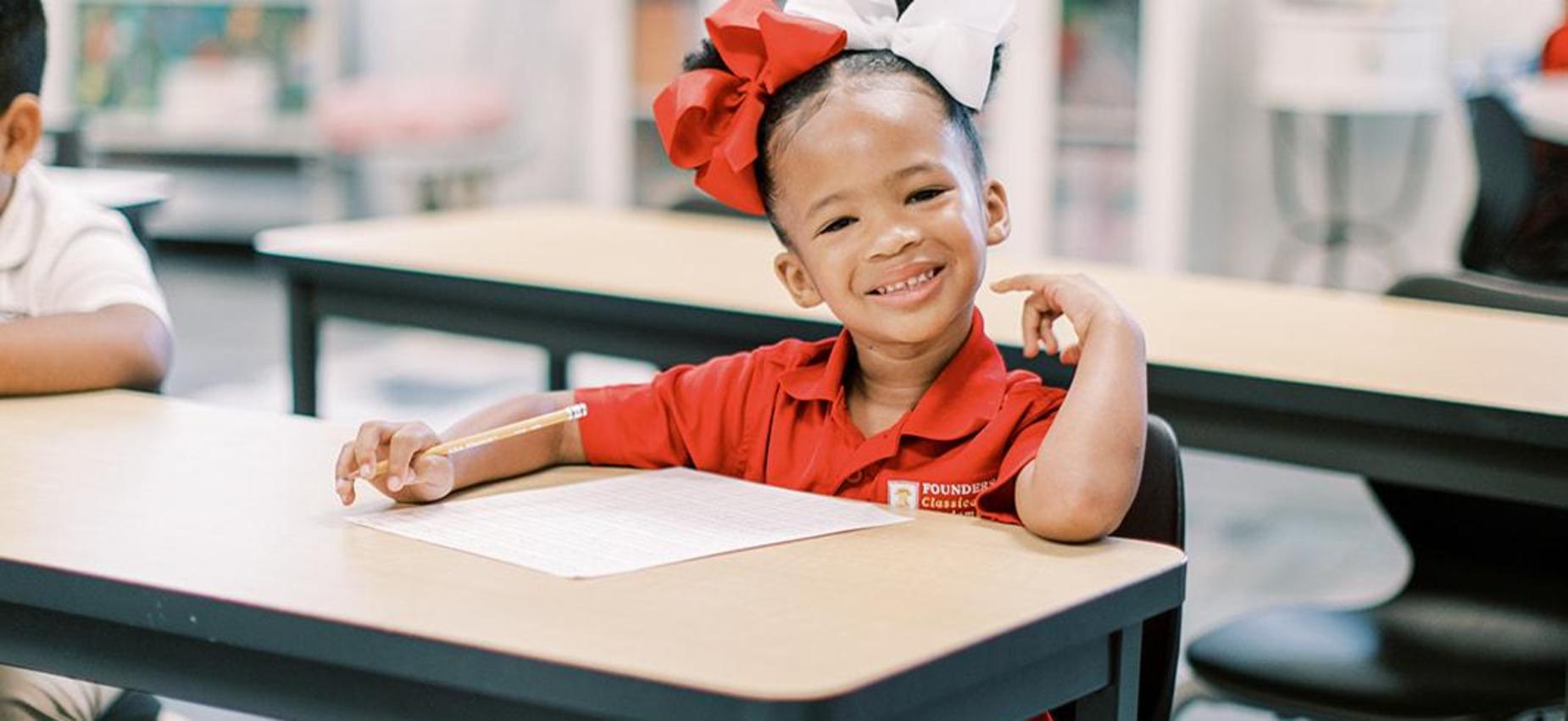 Smiling student with a red hair bow sitting at her desk