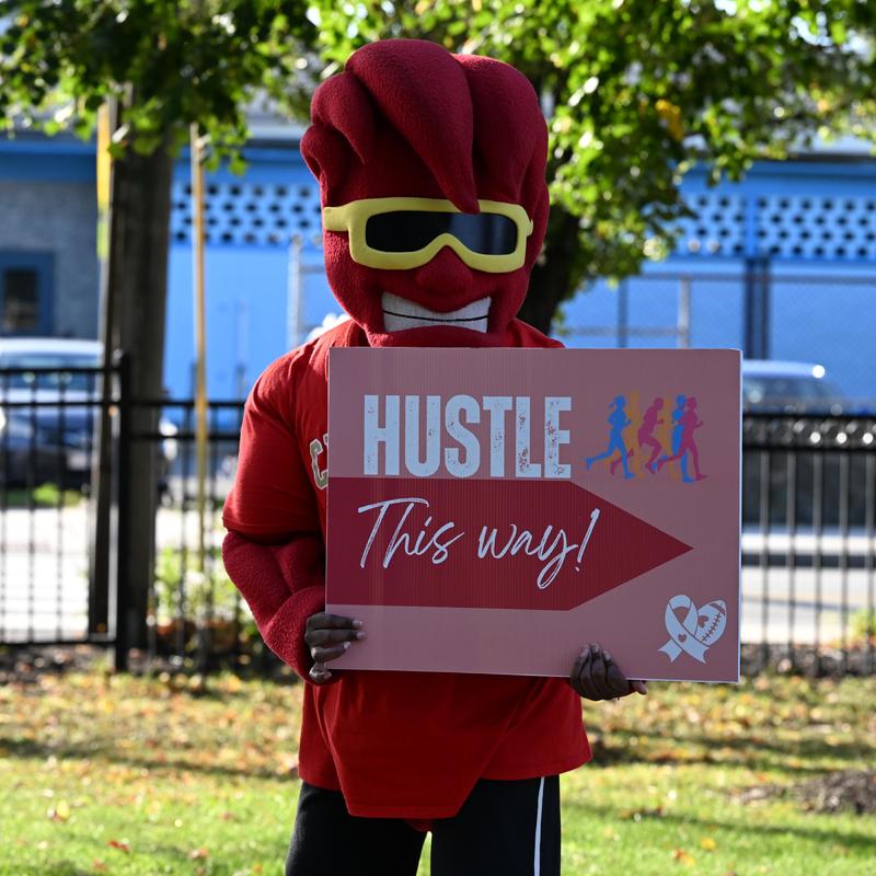 A person in a mascot costume holding a sign directing to a running event.