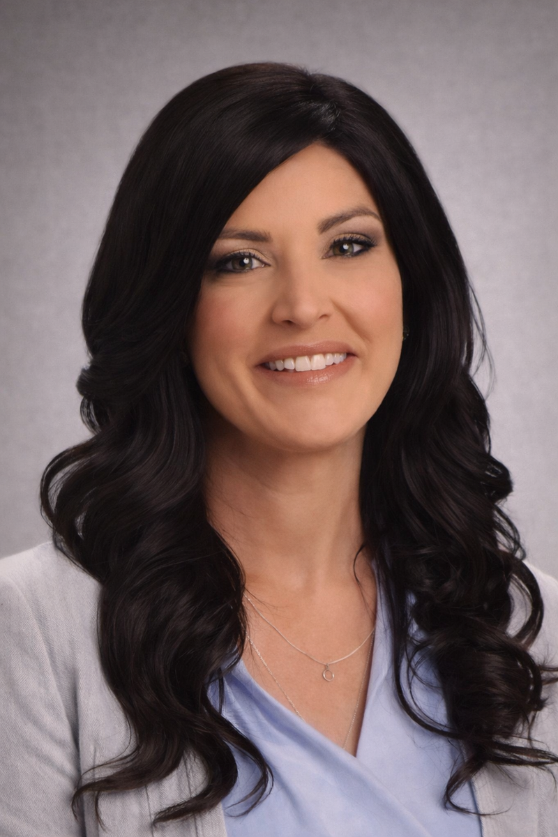 woman with long dark hair with a slight wave smiling at camera in blue shirt and cardigan