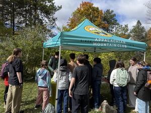 A group of people gathering under a tent for an event in nature.