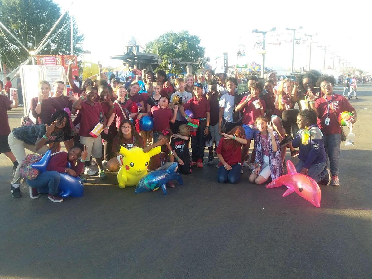 Group of children at a fair, posing with colorful toys and smiling.