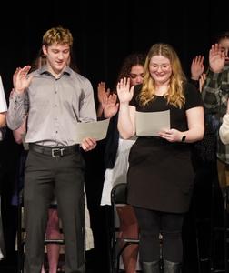 Two students raise their hands as they recite the oath of NHS.