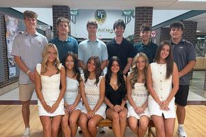 A group of twelve students sit and stand in the high school entryway