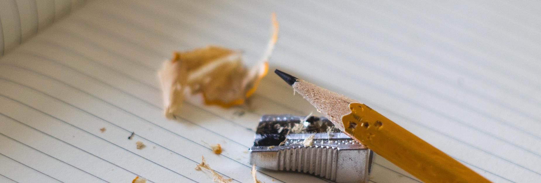 A sharpened pencil, a sharpener, and shavings on a lined notebook.
