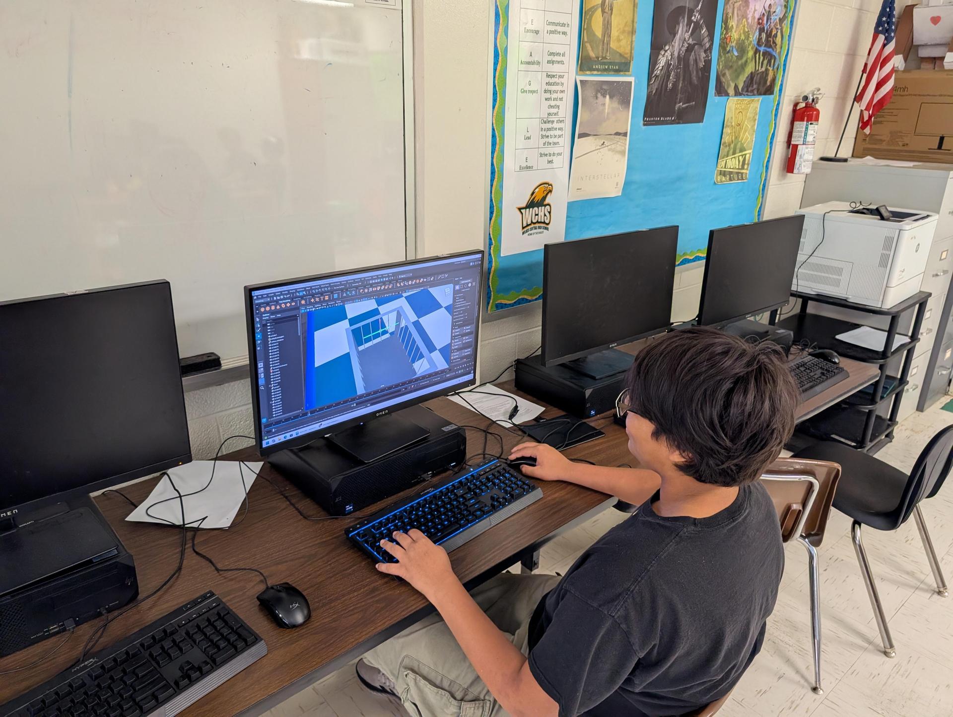 A student focused on a computer screen in a classroom with several other computers.