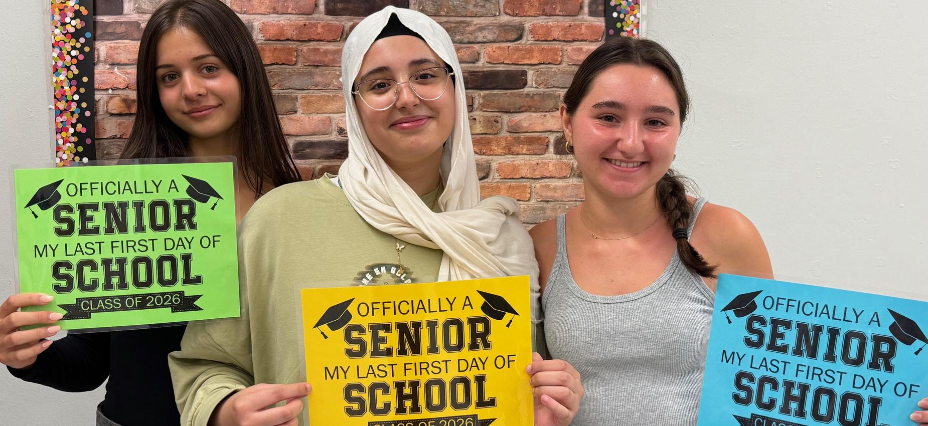 3 students holding "Officially a senior/ My last first day of school" signs