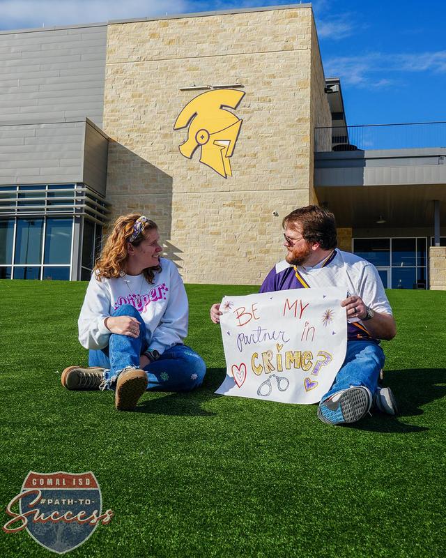 Sam and Mandy Pippert sitting outside with a sign that reads "be my partner in crime?"