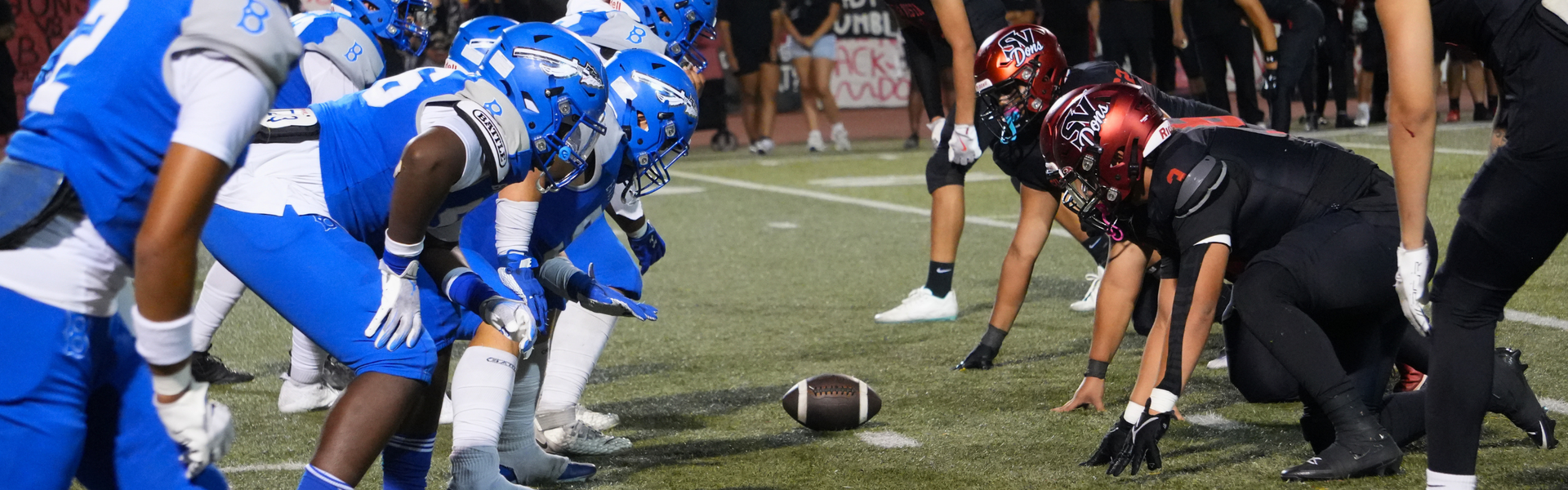 Two football teams face off at the line of scrimmage on a field.