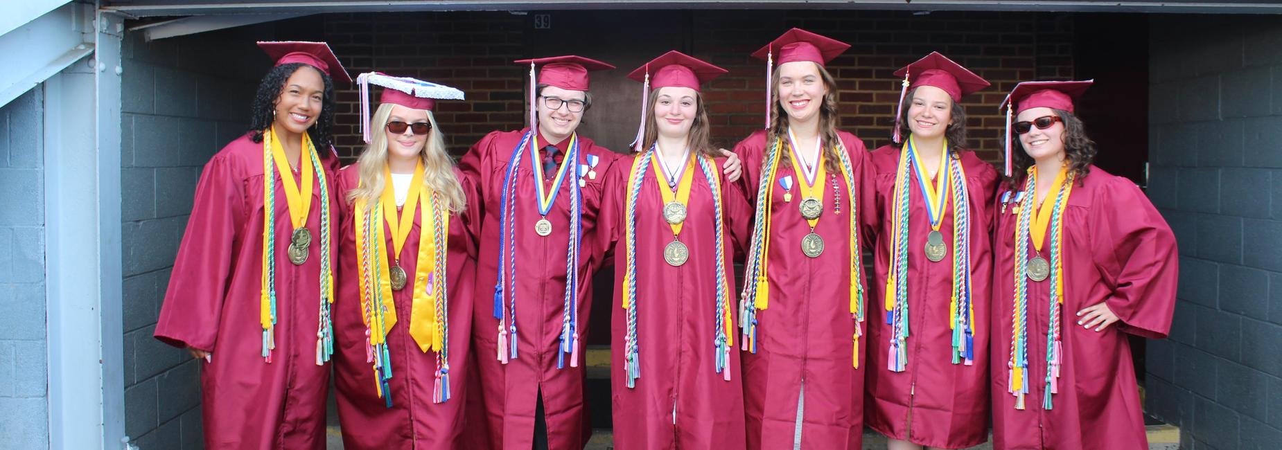 Group of graduating students in maroon caps and gowns, smiling together.