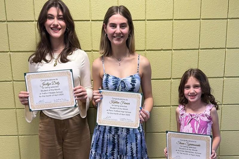 The three students of the month stand holding their certificates at the school board meeting