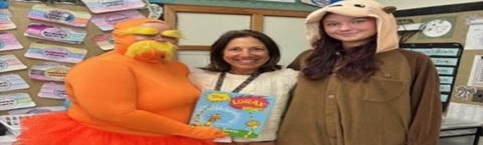 Three people in costumes pose together, holding a children's book.