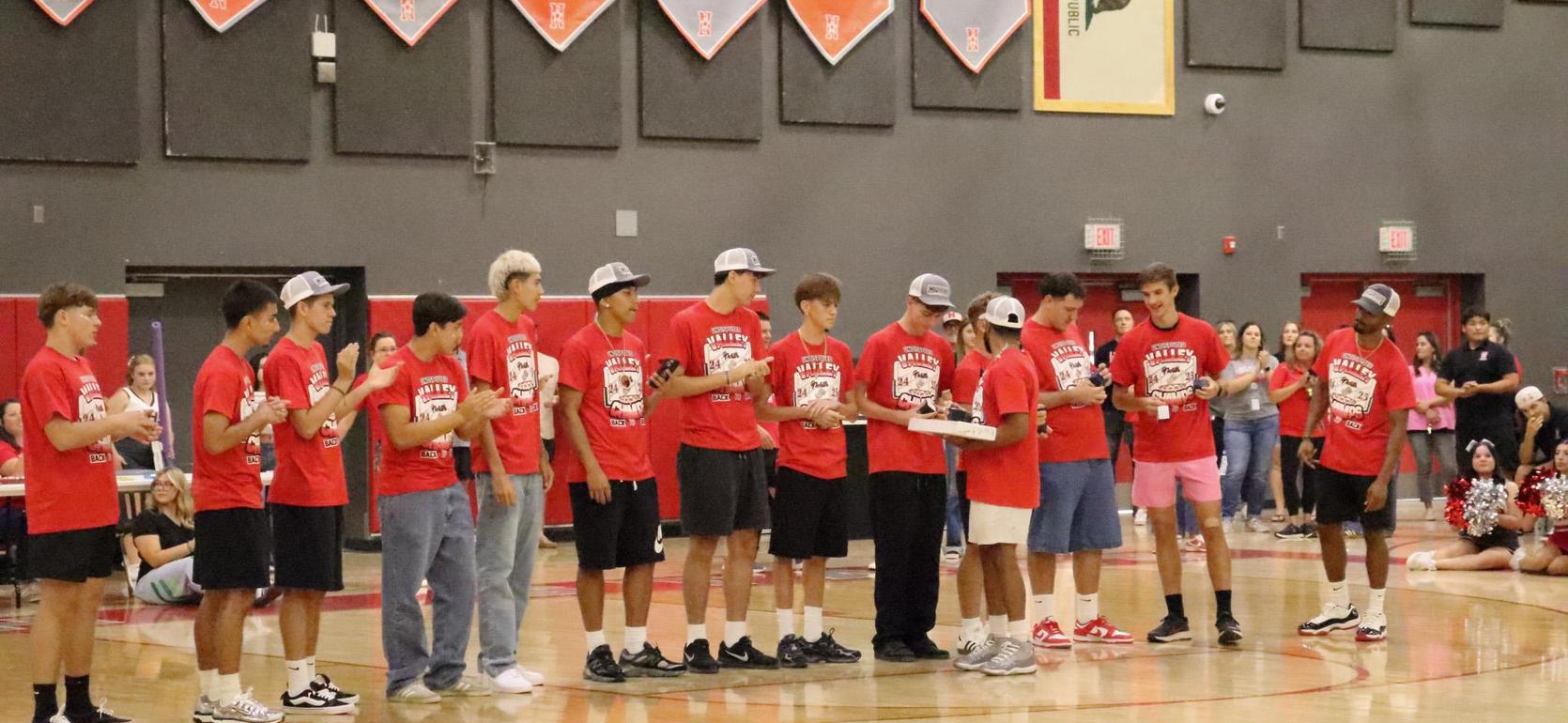 A group of boys in red shirts and caps standing in a gym during an event.