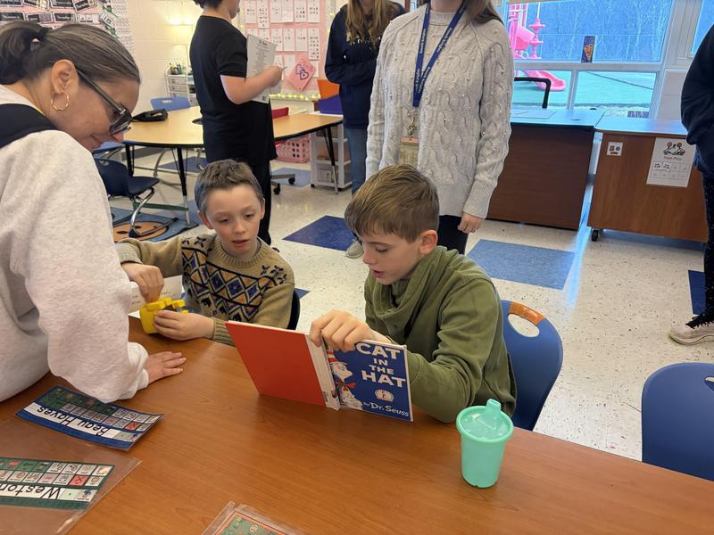 student at table reading dr.suess book to another student