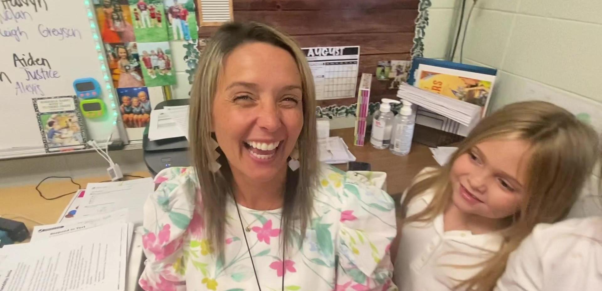 A smiling teacher and a child in an office with paperwork.