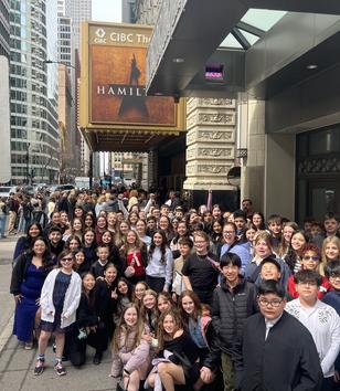 A large group of people poses together outside the CIBC Theatre, promoting 'Hamilton'.