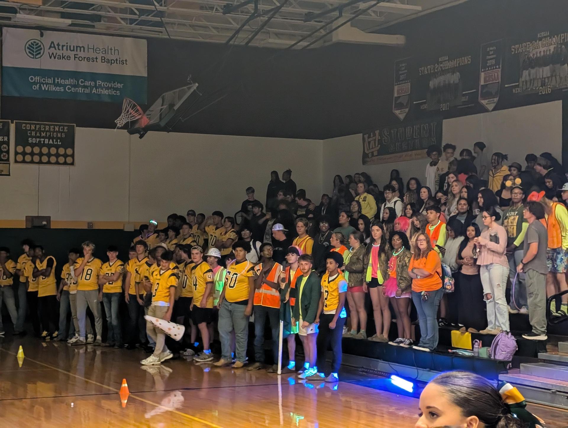 A large crowd of students in yellow jerseys cheering enthusiastically at a school event.