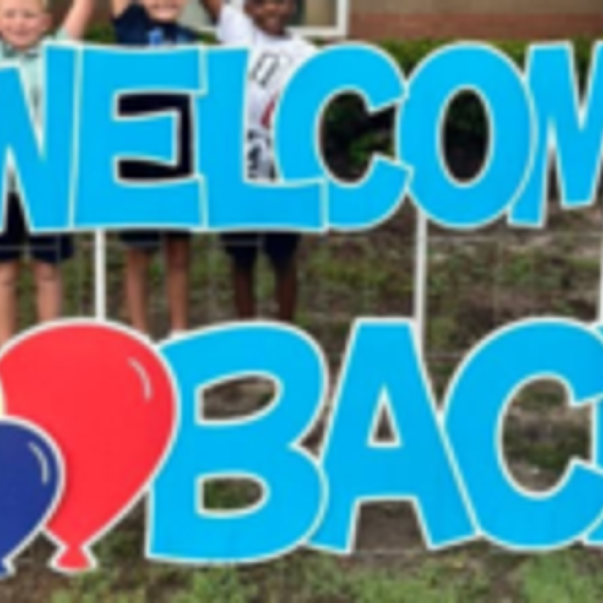 Bright blue 'WELCOME BACK' sign with children smiling behind it.