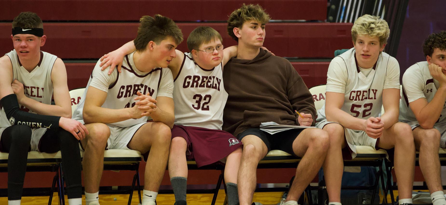 A basketball team sits on the bench, displaying camaraderie and team spirit.