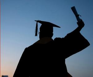 Silhouette of a student in a graduation cap and gown celebrating by holding their hand in the air