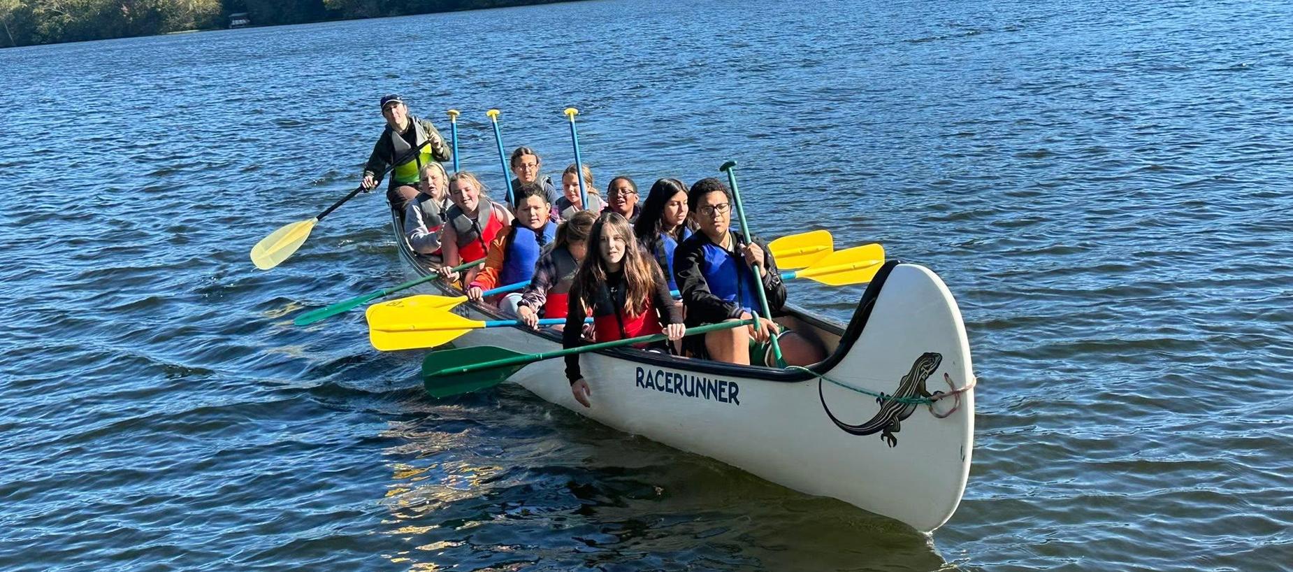 A group of people paddling a large canoe on a serene body of water.