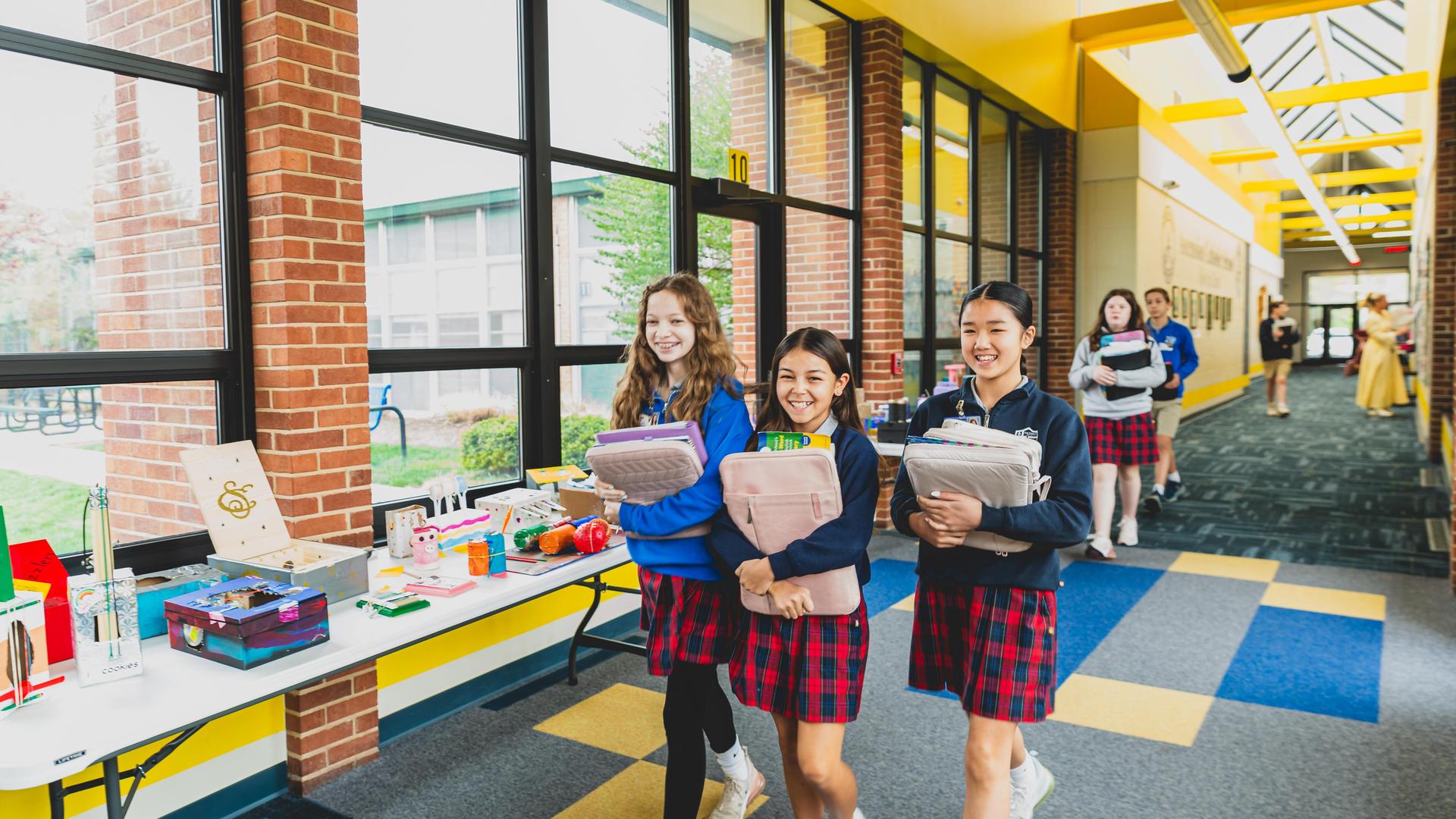 Students in uniforms, carrying books and supplies in a school hallway.