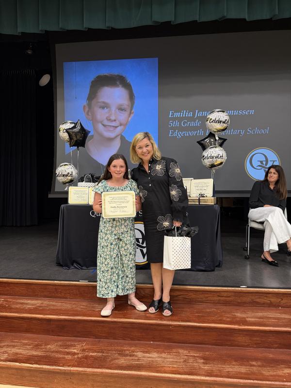 Student holding a certificate is standing between her principal and superintendent on a stage.