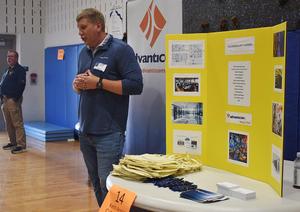A man presenting information at a table with a yellow display board
