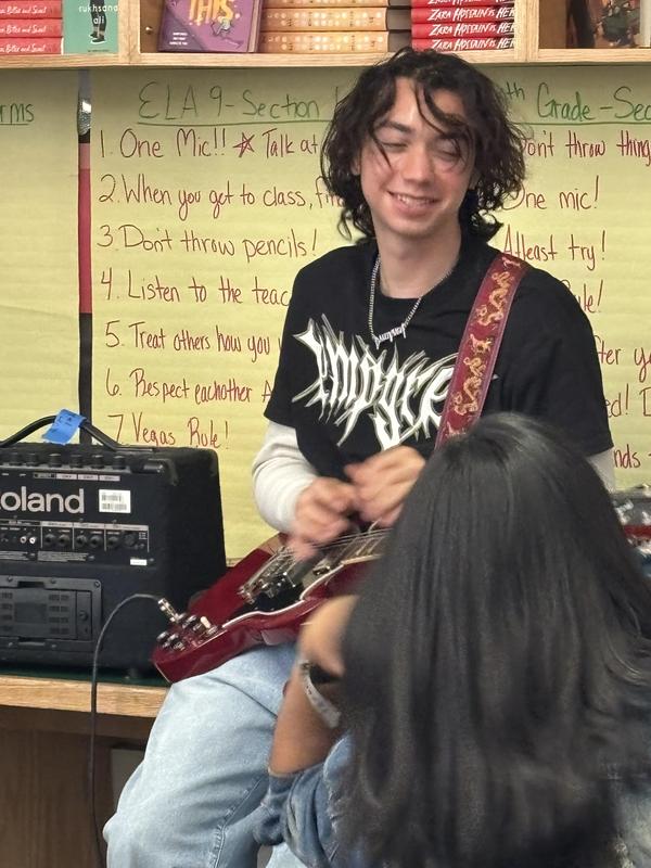 Teen playing guitar in front of a classroom with notes on the wall.