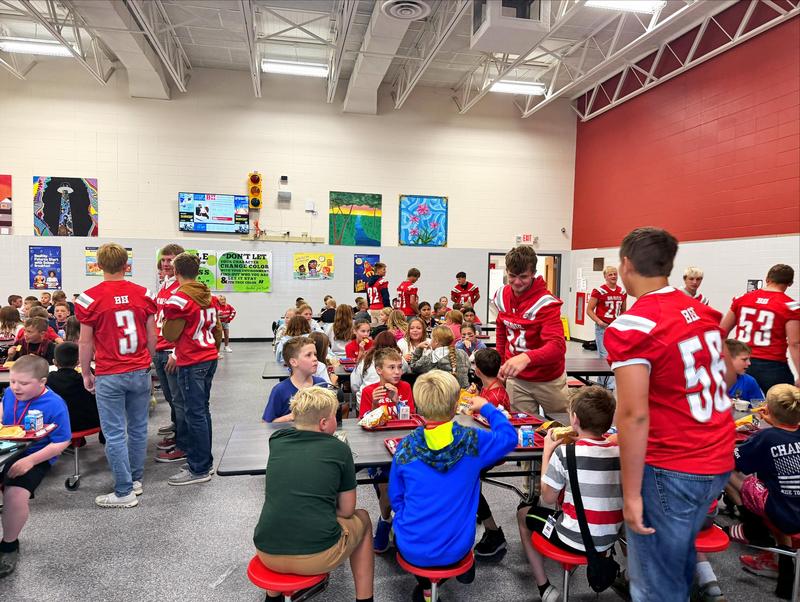 Football players eat with elementary lunch