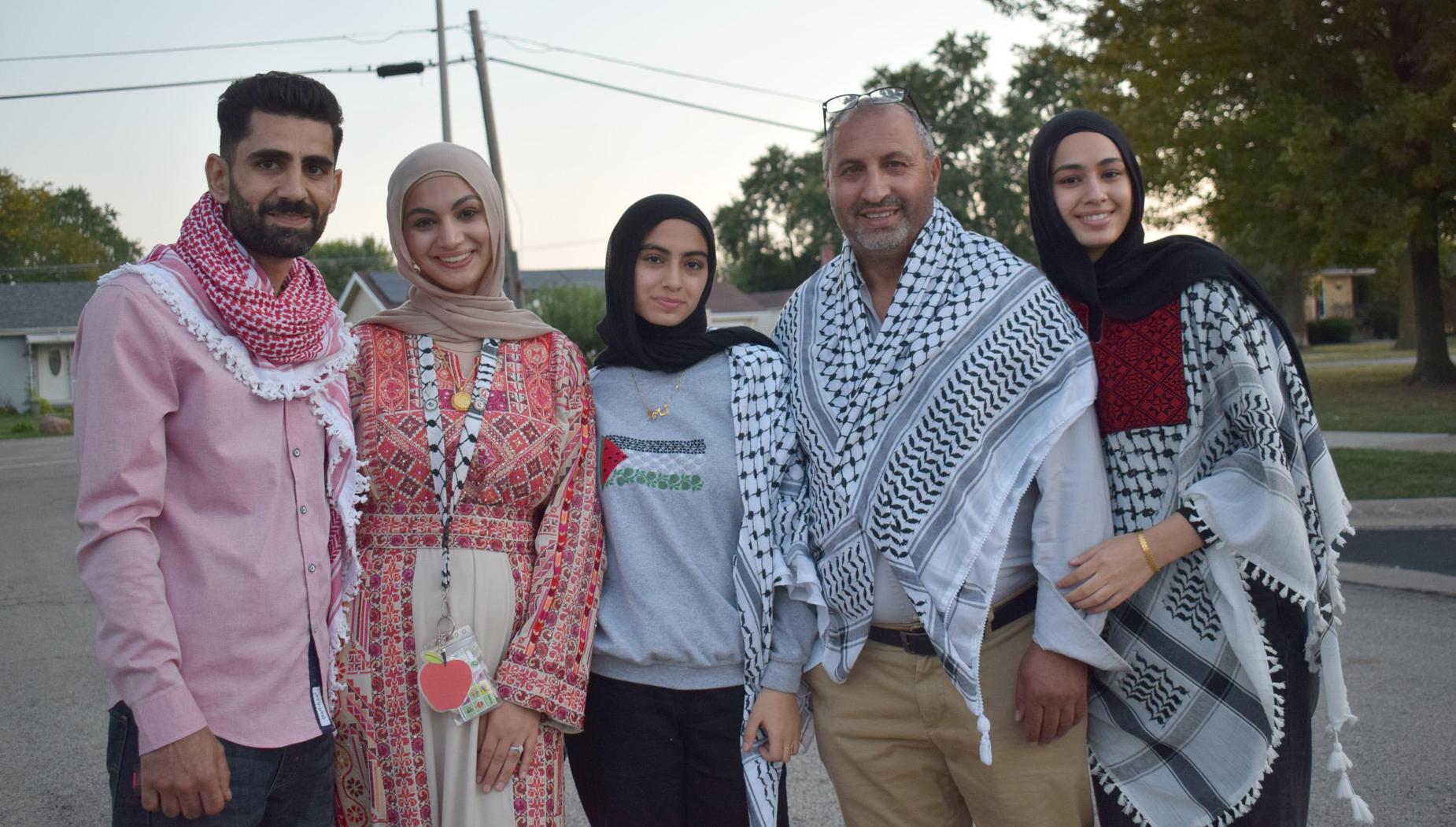 A family of five dressed in traditional attire, smiling outdoors during sunset.