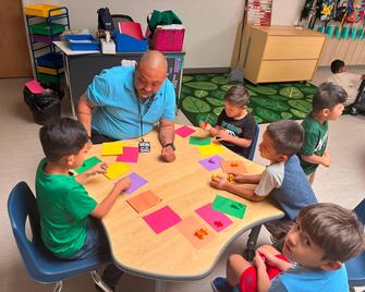 Teacher engages with young children at a colorful learning table.
