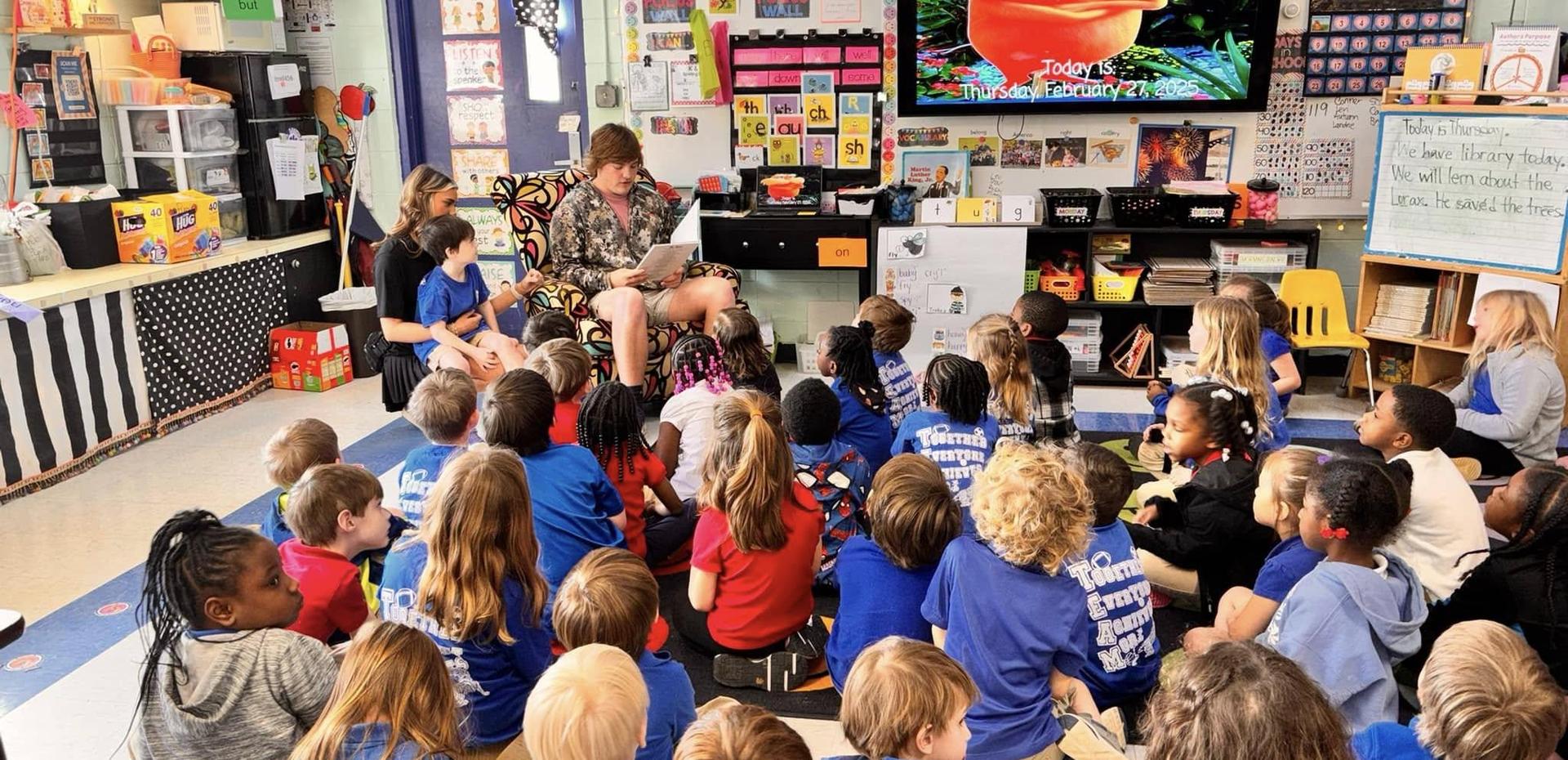 A teacher reading to a diverse group of young students seated on the carpet in a classroom.