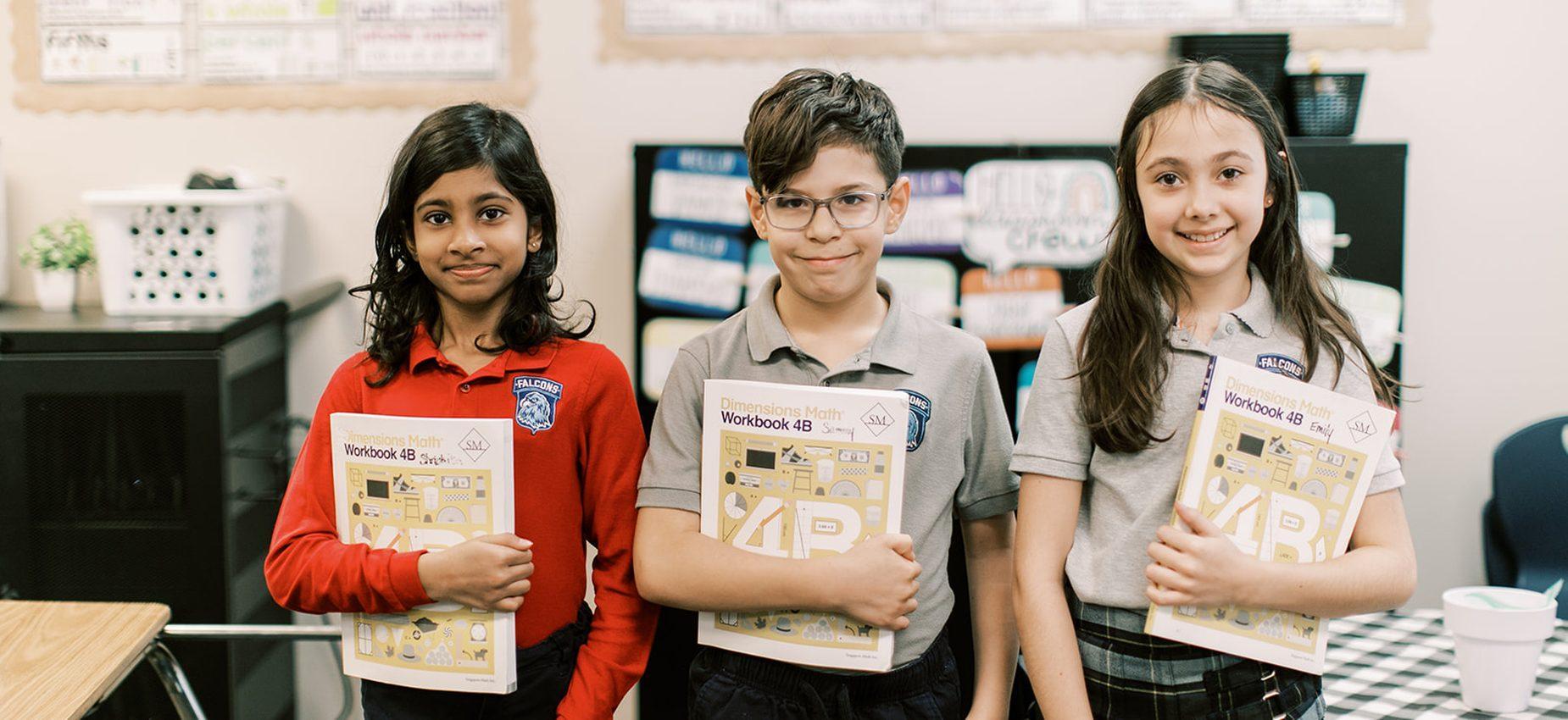 Three Coppell Classical Academy students smile while holding their Singapore math workbooks