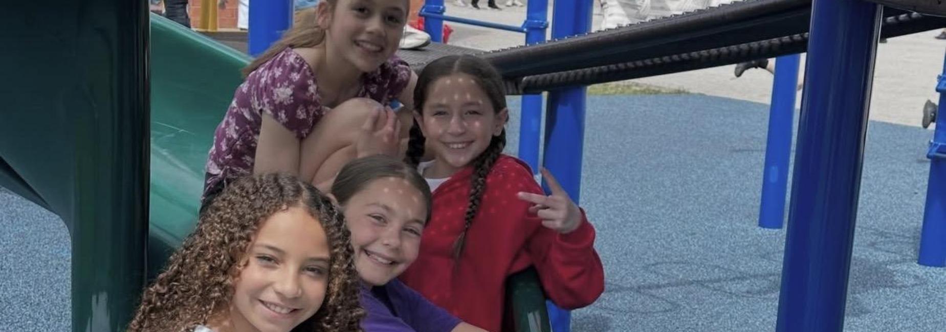 Three children sitting on a slide, smiling and posing for the camera.