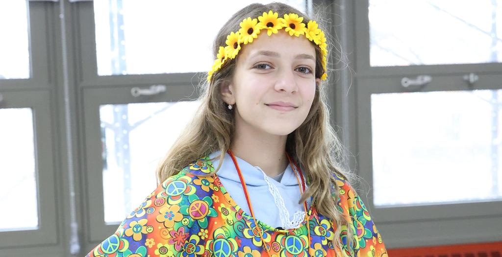 A girl standing with hand on her hip, with a multicolored poncho and daisy headband.