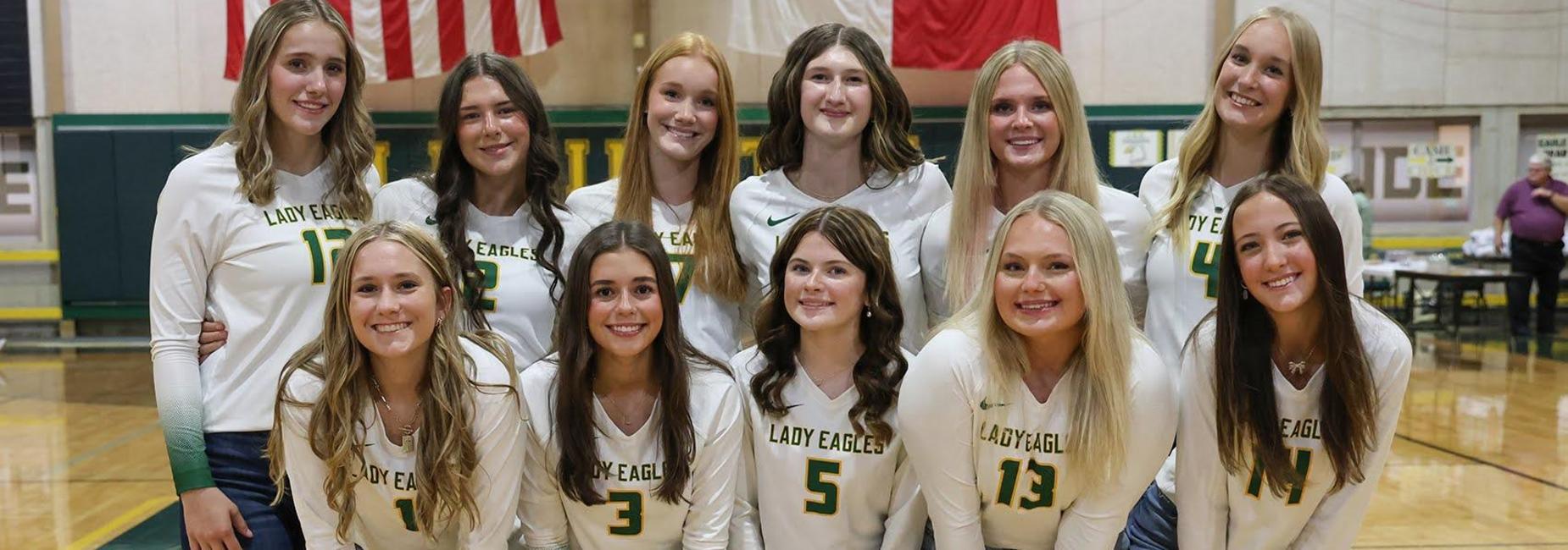 A group of six female volleyball players in matching uniforms, smiling and posing.
