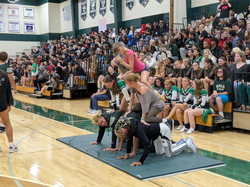 Students performing a stunt during a school event with a large crowd in the background.