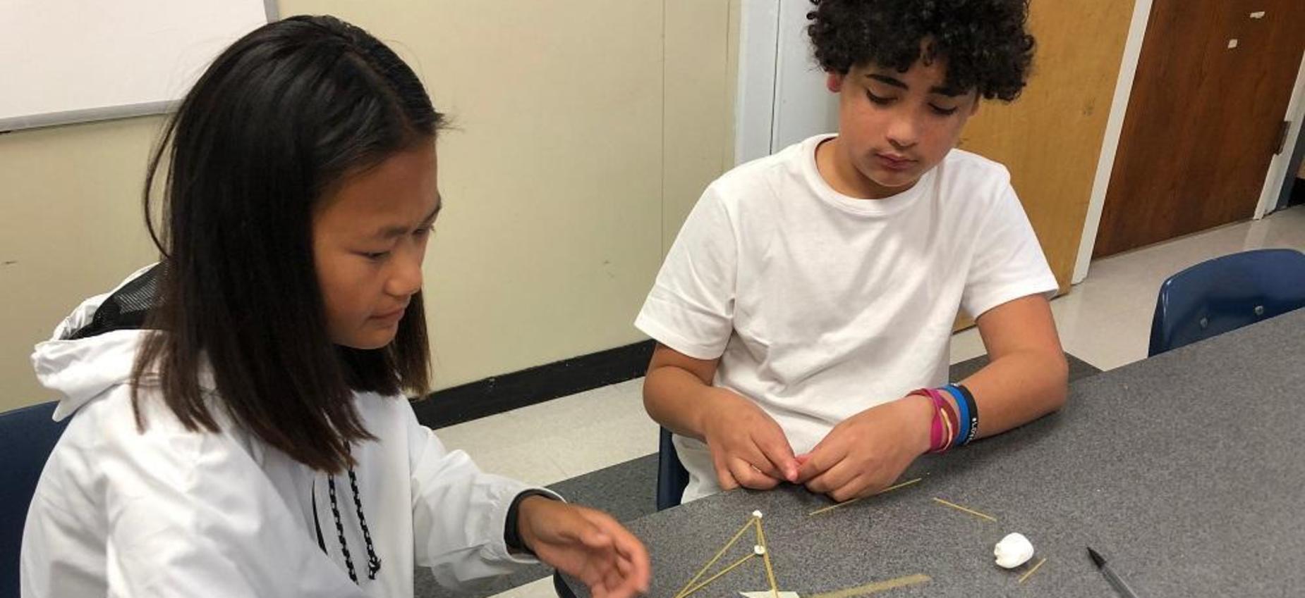 Two students work on a project at a table.