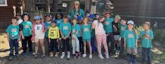 A large group of children in matching shirts stands outside with an instructor.