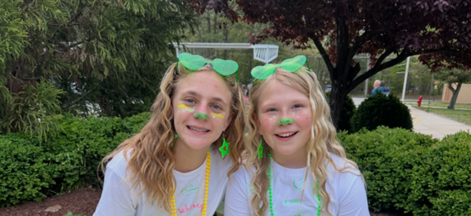 Two girls in green tutus and T-shirts, smiling and covered in colorful paint.