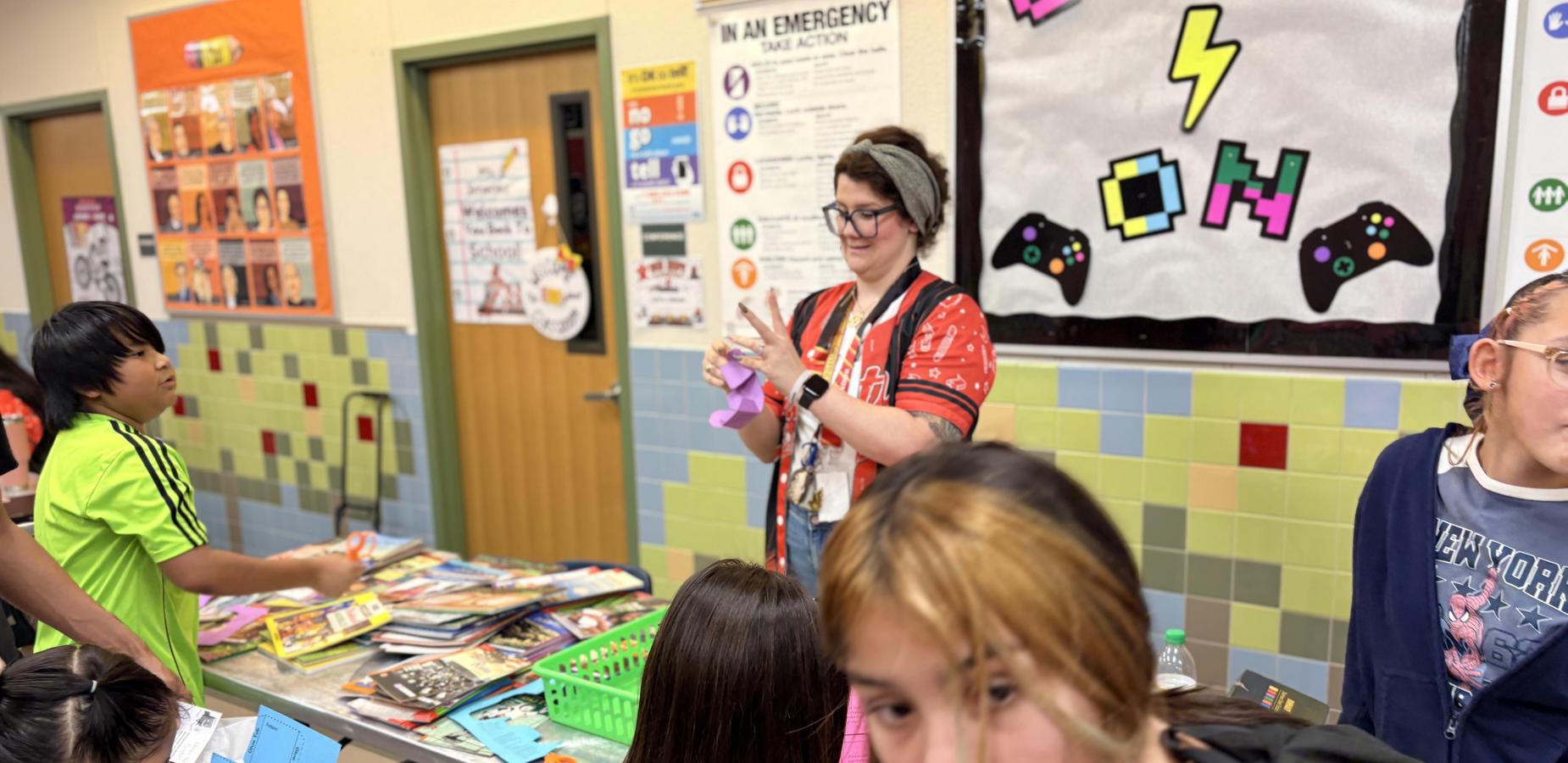 Students gather around a table with books and a teacher facilitating an activity.