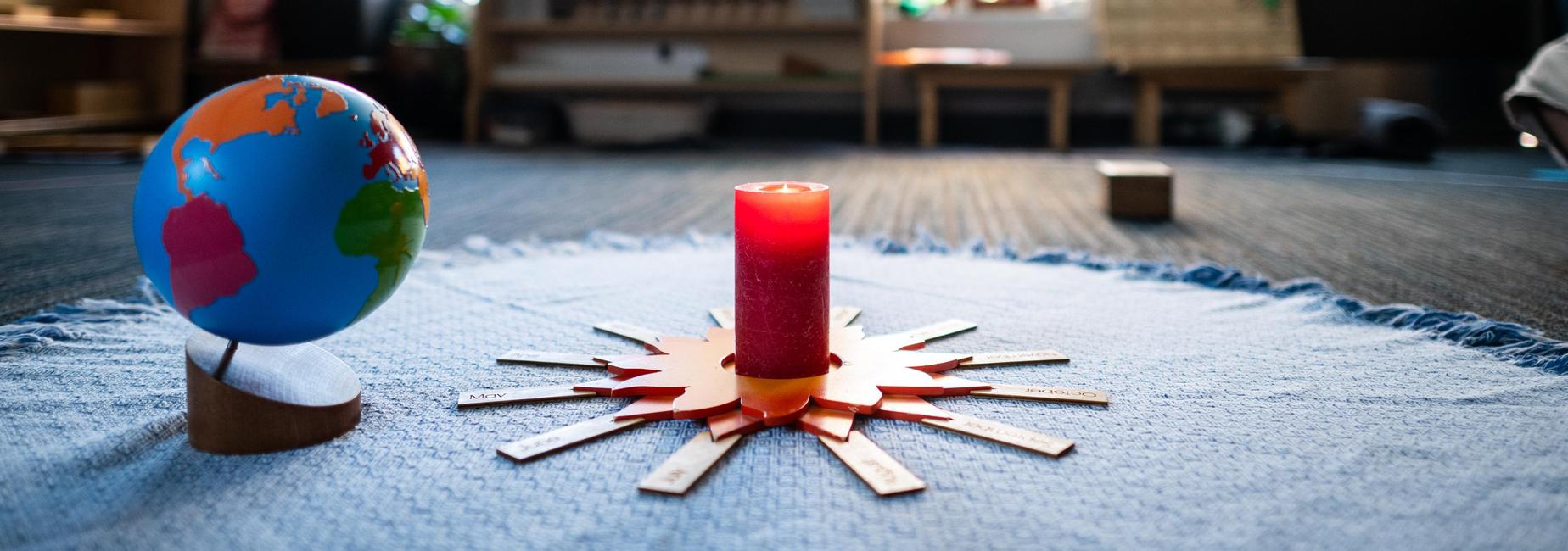 A globe and red candle on a blue cloth in a classroom setting.