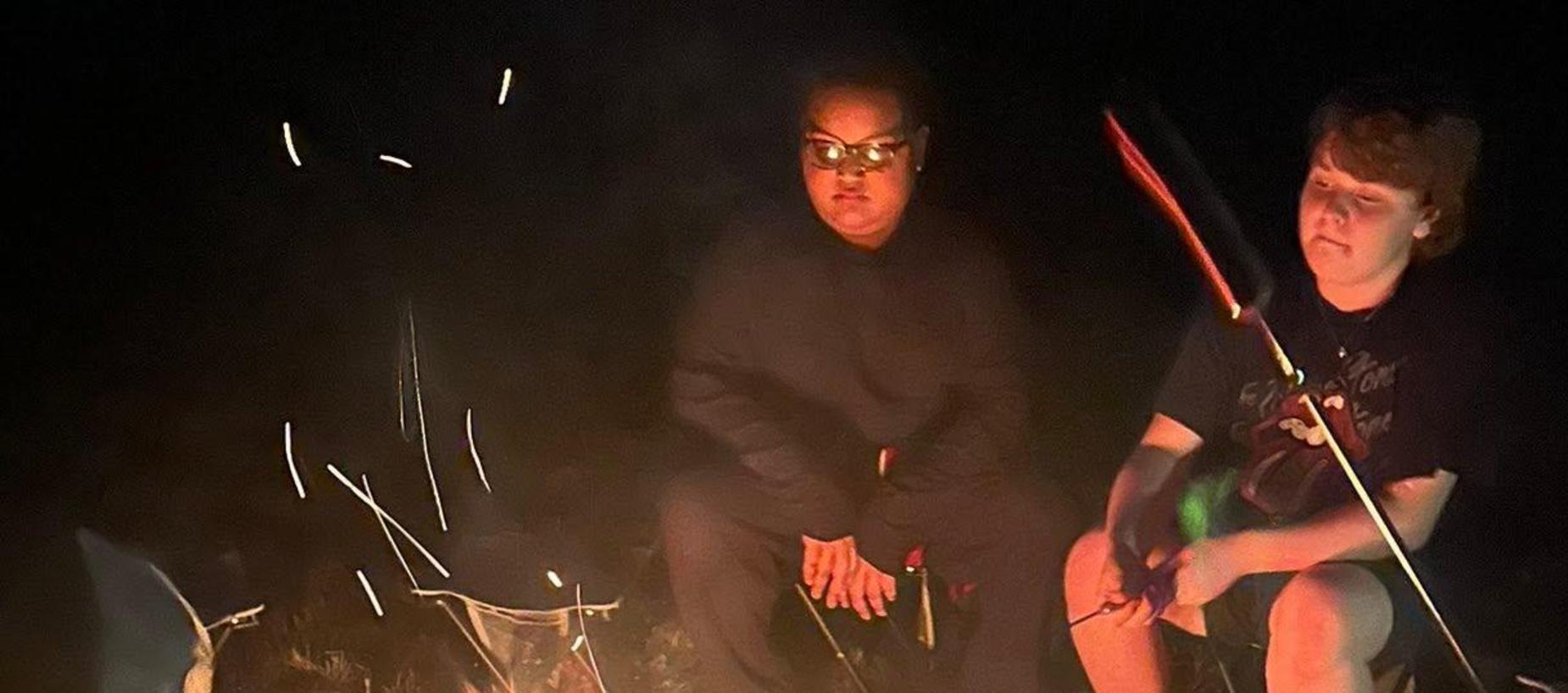 A campfire surrounded by people sitting on the ground at night.