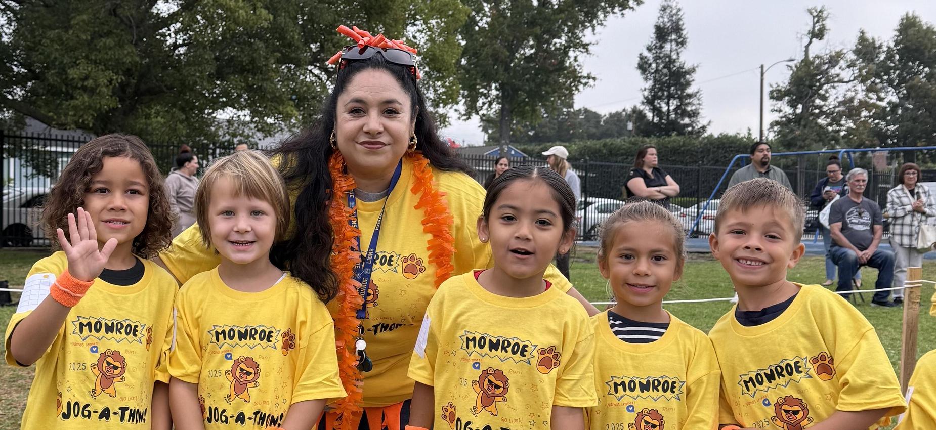 Group of children in yellow shirts smiling with an adult, at a jog-a-thon event.