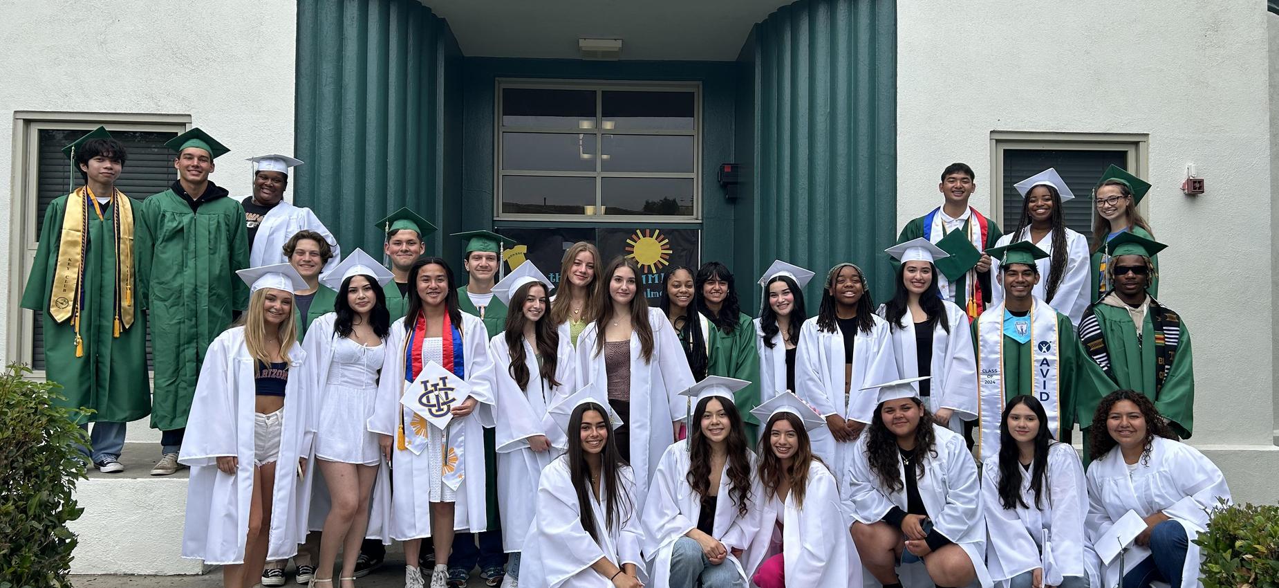 Group of diverse students in graduation attire posing in front of a building.